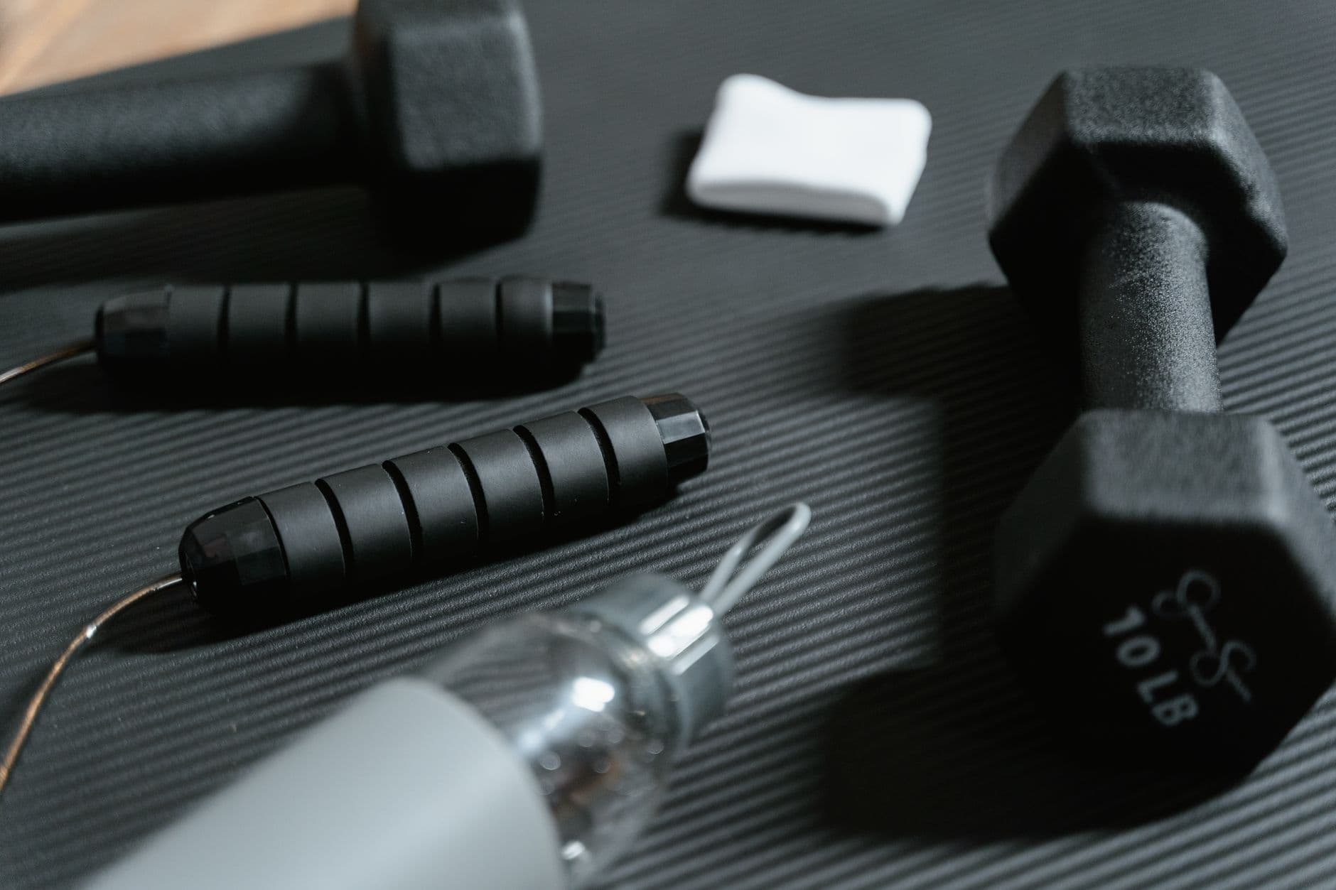 Dumbbells, jumping rope, and water bottle on a yoga mat for home workout routine.