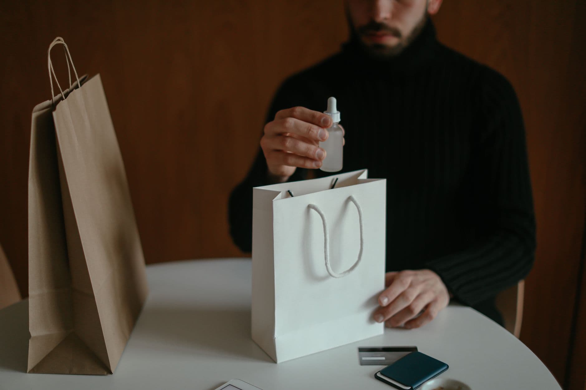 Crop unrecognizable guy with beard in casual clothes sitting at table and checking delivered goods after placing online order