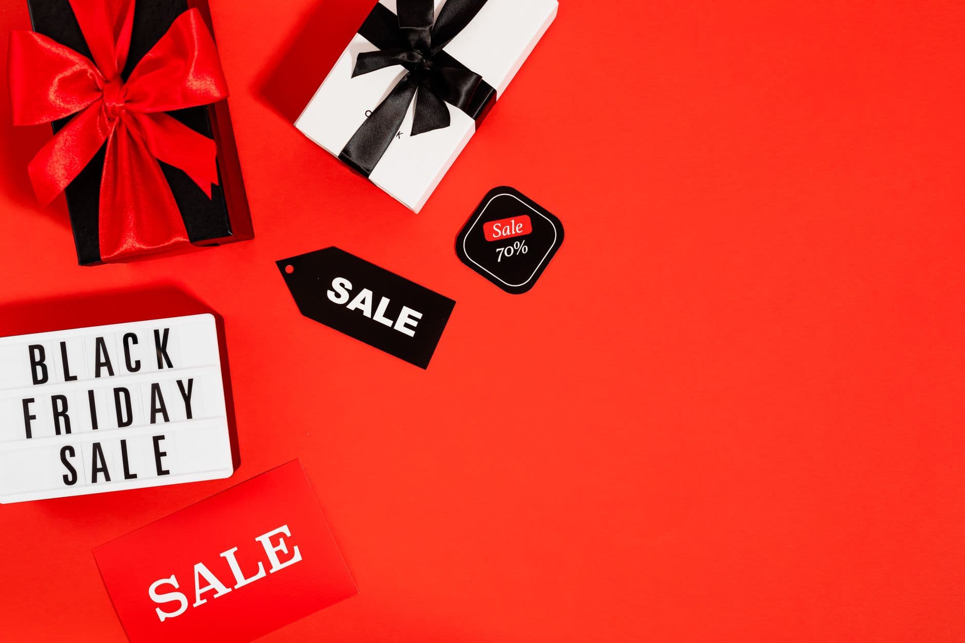 Flatlay of Black Friday sale gifts and tags on a red background with ample copy space.